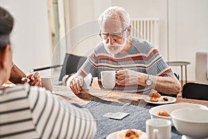 Senior man holding cup of tea and playing at the cards