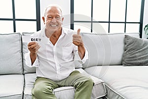 Senior man holding diet banner smiling happy and positive, thumb up doing excellent and approval sign