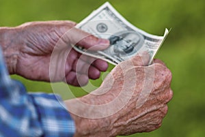 Senior man holding dollar banknotes, closeup of elderly male hands with hundred dollar bills