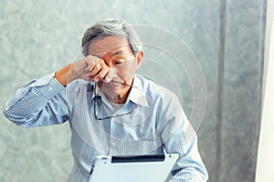 Senior man is holding eyeglasses and rubbing his tired eyes whi