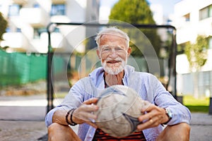 Senior man holding football in hands. Older, vital man has active lifestyle, doing sport every day.