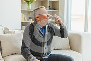 Senior man holding glass drinking fresh water at home. Mature old senior thirsty grandfather takes care of his health