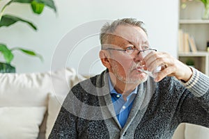 Senior man holding glass drinking fresh water at home. Mature old senior thirsty grandfather takes care of his health