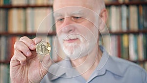 Senior man holding and looking at cryptocurrency bitcoin. Shiny virtual money of online trade