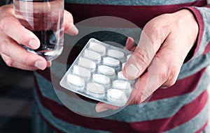 Senior man holding a pack of pills and a glass of water in his hands. Caring for the health of the elderly. Close-up