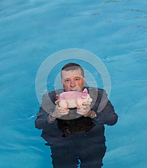 Senior man holding piggy bank above water