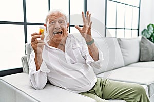 Senior man holding pills crazy and mad shouting and yelling with aggressive expression and arms raised