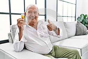 Senior man holding pills doing happy thumbs up gesture with hand