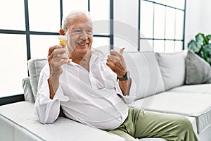Senior man holding pills smiling with happy face looking and pointing to the side with thumb up