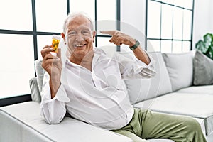 Senior man holding pills smiling pointing to head with one finger, great idea or thought, good memory