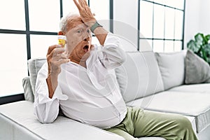 Senior man holding pills surprised with hand on head for mistake, remember error