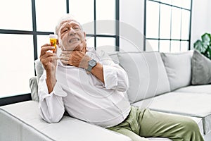 Senior man holding pills touching painful neck, sore throat for flu, clod and infection