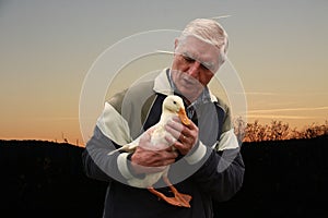 A senior man holding and talking to a duck
