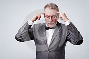 Senior man holds fingers on temples, trying to remember