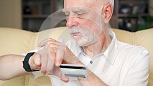 Senior man at home buying online with credit card on smartwatch. Technology use by older people