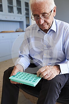 Senior Man At Home Using Pill Organiser For Medication
