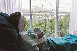 Senior man on a hospital bed alone in a room looking through the hospital window. Elderly patient.