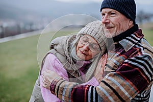 Senior man hugging and consoling his upset wife outdoors in garden in winter.