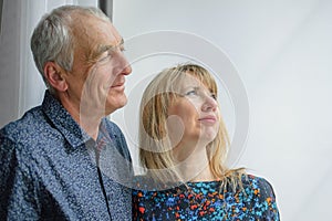 Senior Man Hugging His Young Blond Wife near the Window. Woman Looking at the Camera. Psychology of Relations Concept.