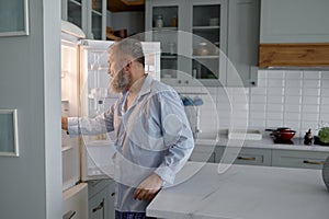 Senior man hunger looking inside open fridge on kitchen