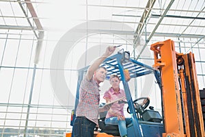 Senior man instructing young female driving forklift in greenhouse