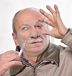 Senior man with irritated red bloodshot eye holding syringe