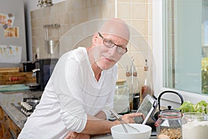 Senior man in kitchen using tablet
