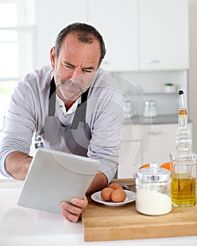 Senior man in the kitchen using tablet