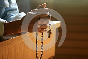 Senior man kneel, holding wooden rosary beads in hand with Jesus Christ holy cross crucifix in the church.