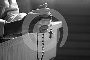 Senior man kneel, holding wooden rosary beads in hands with Jesus Christ holy cross crucifix in the church. Natural light