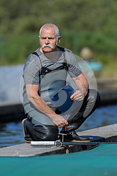 senior man knelt by water enclosure wearing waders photo