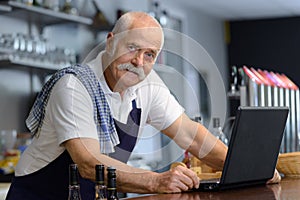 senior man with laptop working behind bar