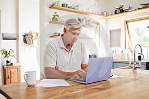 Senior man, laptop and working in kitchen on retirement plan, budget and expenses at home. Elderly male typing on