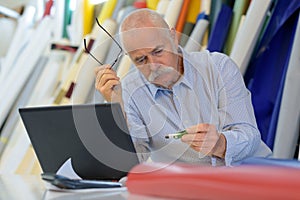 senior man with laptop in workplace examining usb flash key