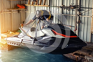 Senior man launching or lifting modern fast jetski hanged on strpas with wire hoist rail crane for dry storage. Boat garage