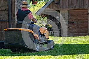 A senior man with a lawn mower mows the grass in the yard of country house