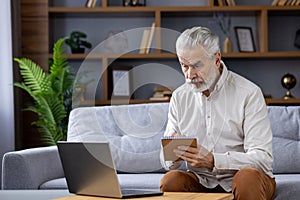 Senior man learns remotely with laptop and notebook at home