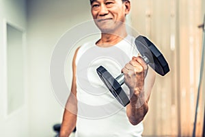 Senior man lifting dumbbell in fitness gym.