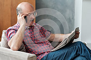 Senior man in living room reading newspaper talking on phone with his children