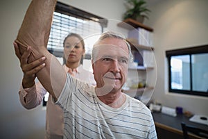 Senior man looking away while female doctor examining elbow