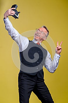 Senior man looking at camera while taking silly face selfie waving to the camera