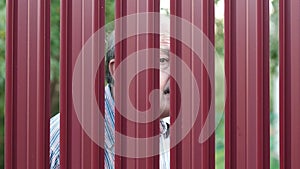 Senior man looking through fence spying on his neighbor