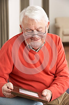 Senior Man Looking At Photograph In Frame