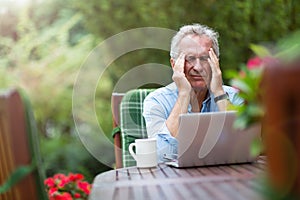 Senior man looking stressed while working on laptop