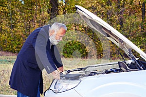 Senior man looking under the hood of breakdown car