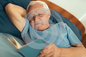 Senior man lying on bad and reading book