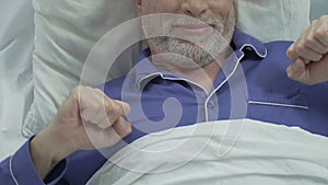 Senior man lying in bed, stretching after waking up, smile on face, sound sleep