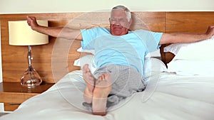 Senior man lying on bed yawning and stretching