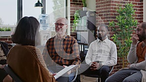 Senior man making confession in front of people at aa group therapy session