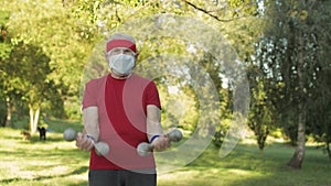 Senior man making fitness exercises with dumbbells during coronavirus virus pandemic alone in park